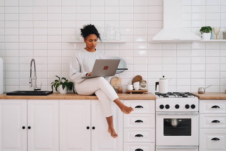 Woman sitting on a kitchen counter using a laptop, enjoying a modern lifestyle.